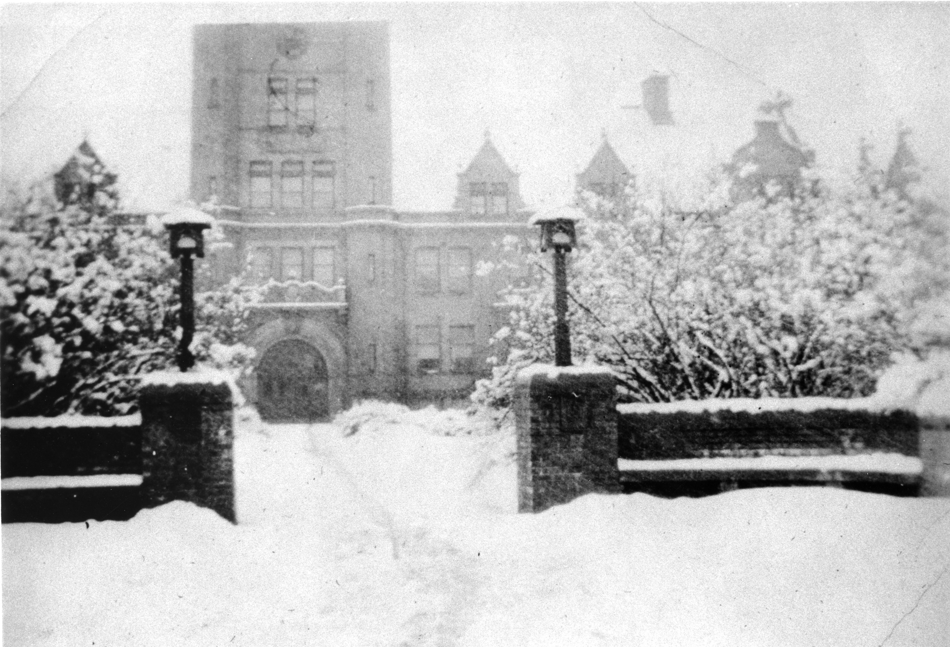 An old black and white photo of the 1909/1910 campus gates with lanterns in front of Liberal Arts Hall (Shilling Hall)