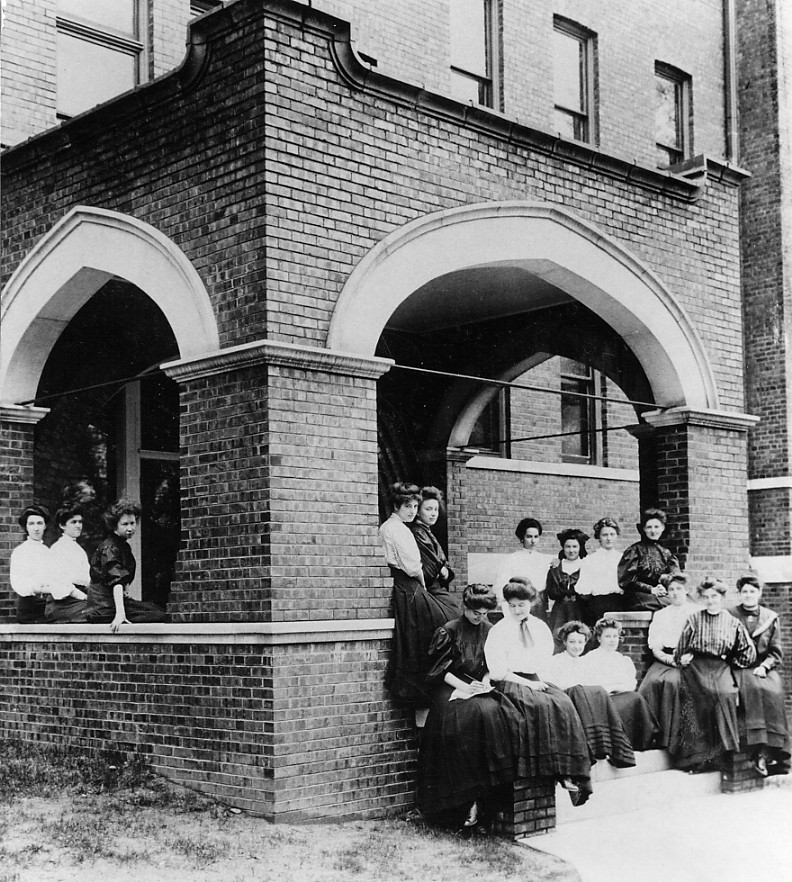 Black and white photo of women students posing on Aston's porch