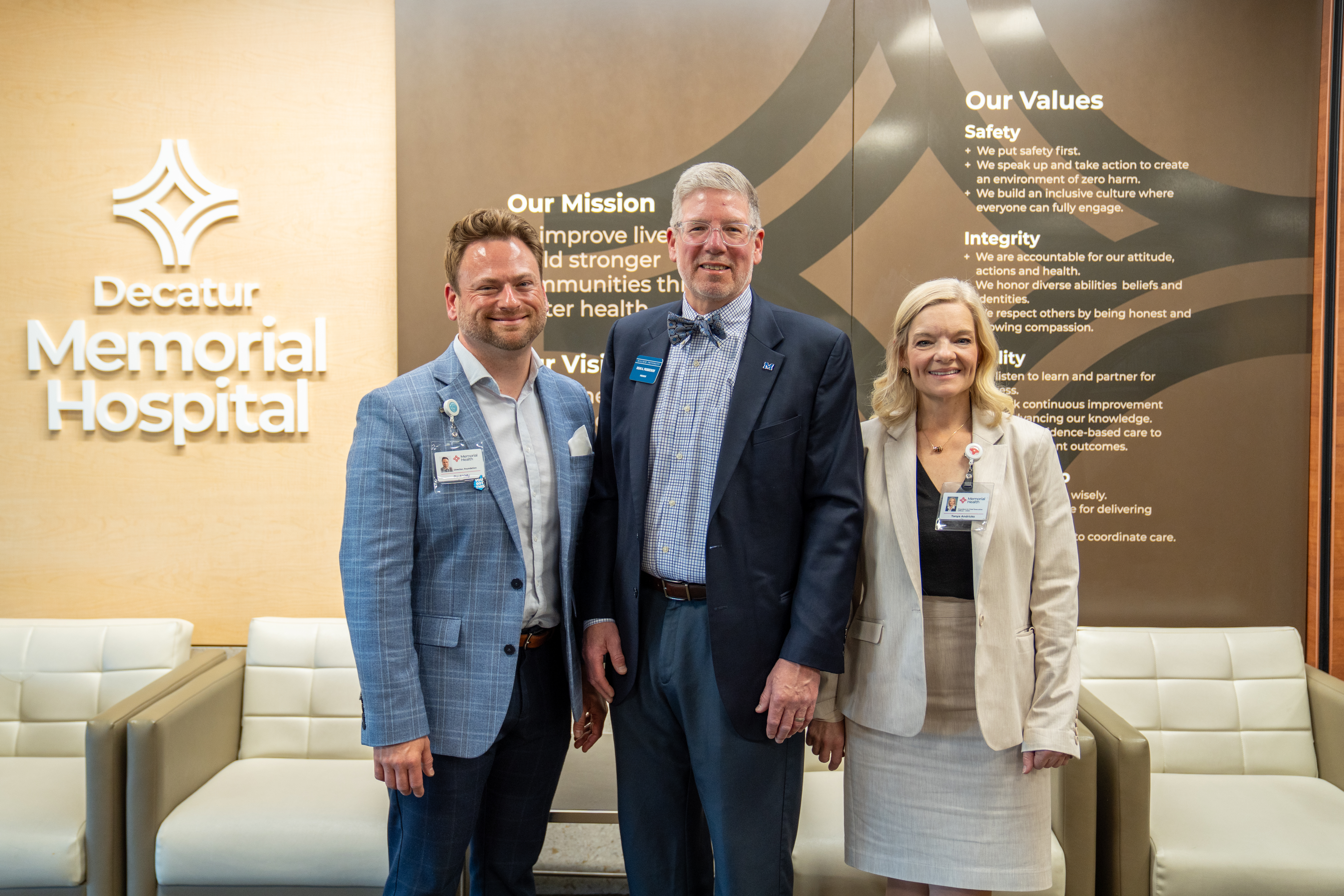 Three business professionals standing in front of a wall reading "Decatur Memorial Hospital"