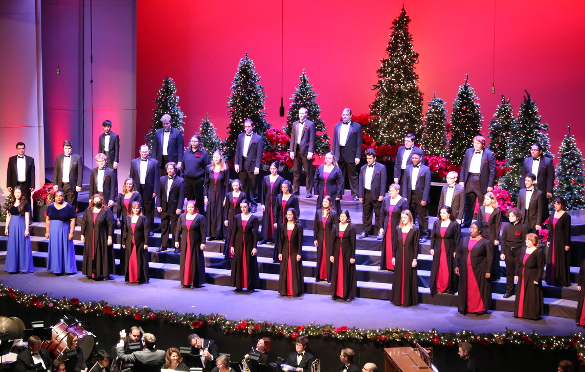 Millikin Choirs sing on Kirkland&#039;s stage for VESPERS. The stage has a red background and is decorated with Christmas trees. 