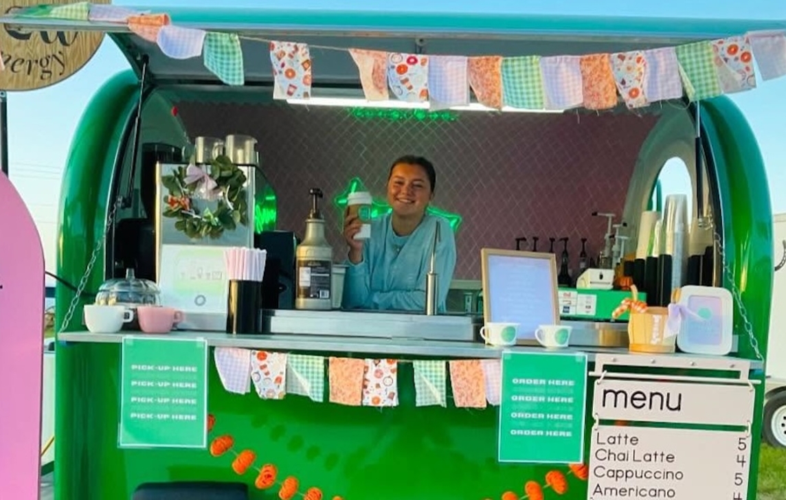 Image of green coffee trailer with young woman posing with beverage