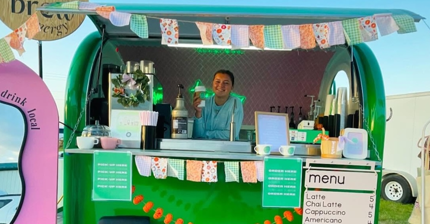 Image of green coffee trailer with young woman posing with beverage