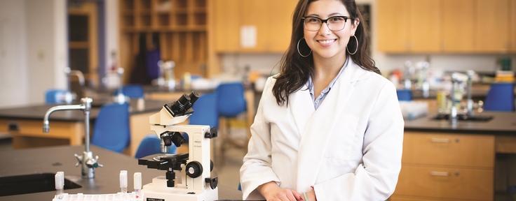 Student smiling next to a microscope