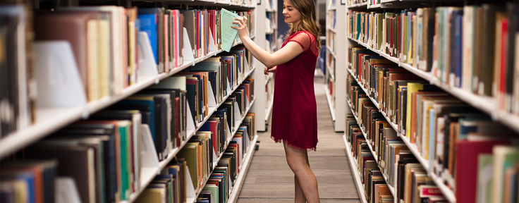 student pulling book from bookshelf