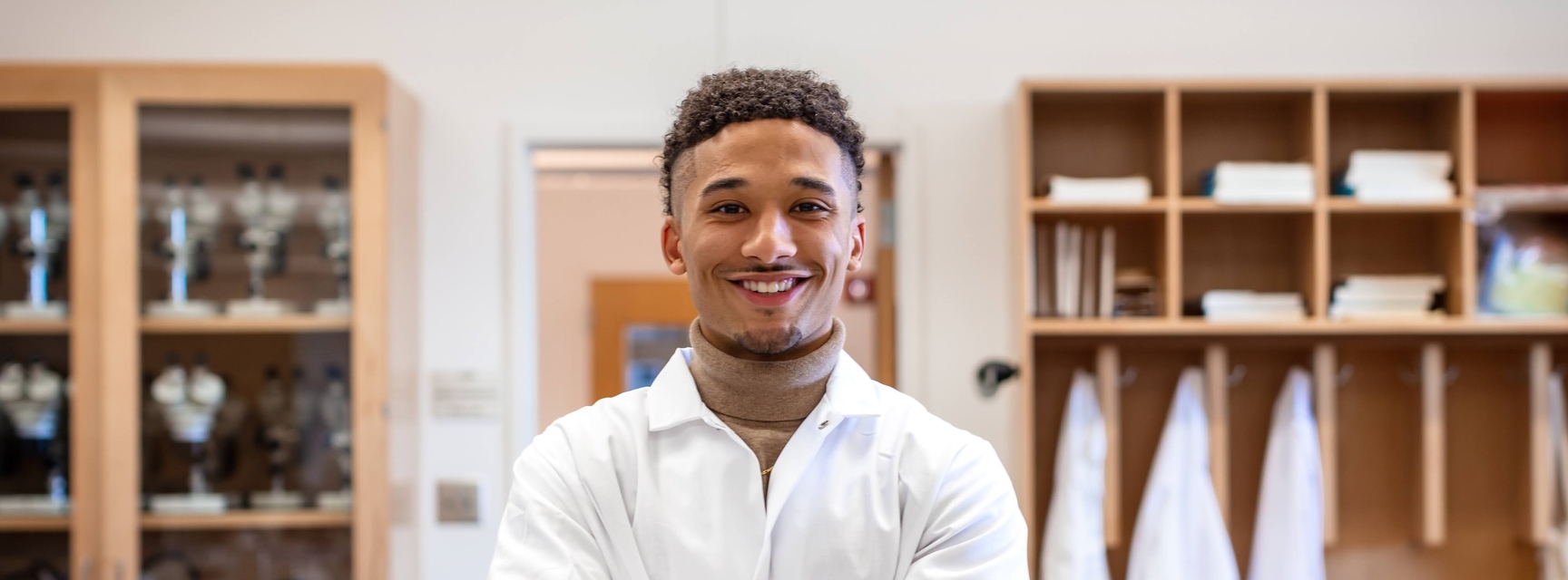 Male student in lab coat smiling at camera