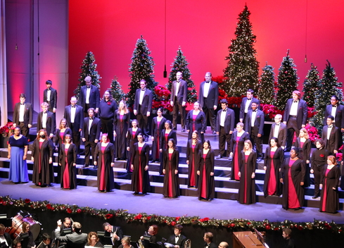 Millikin Choirs sing on Kirkland&#039;s stage for VESPERS. The stage has a red background and is decorated with Christmas trees. 