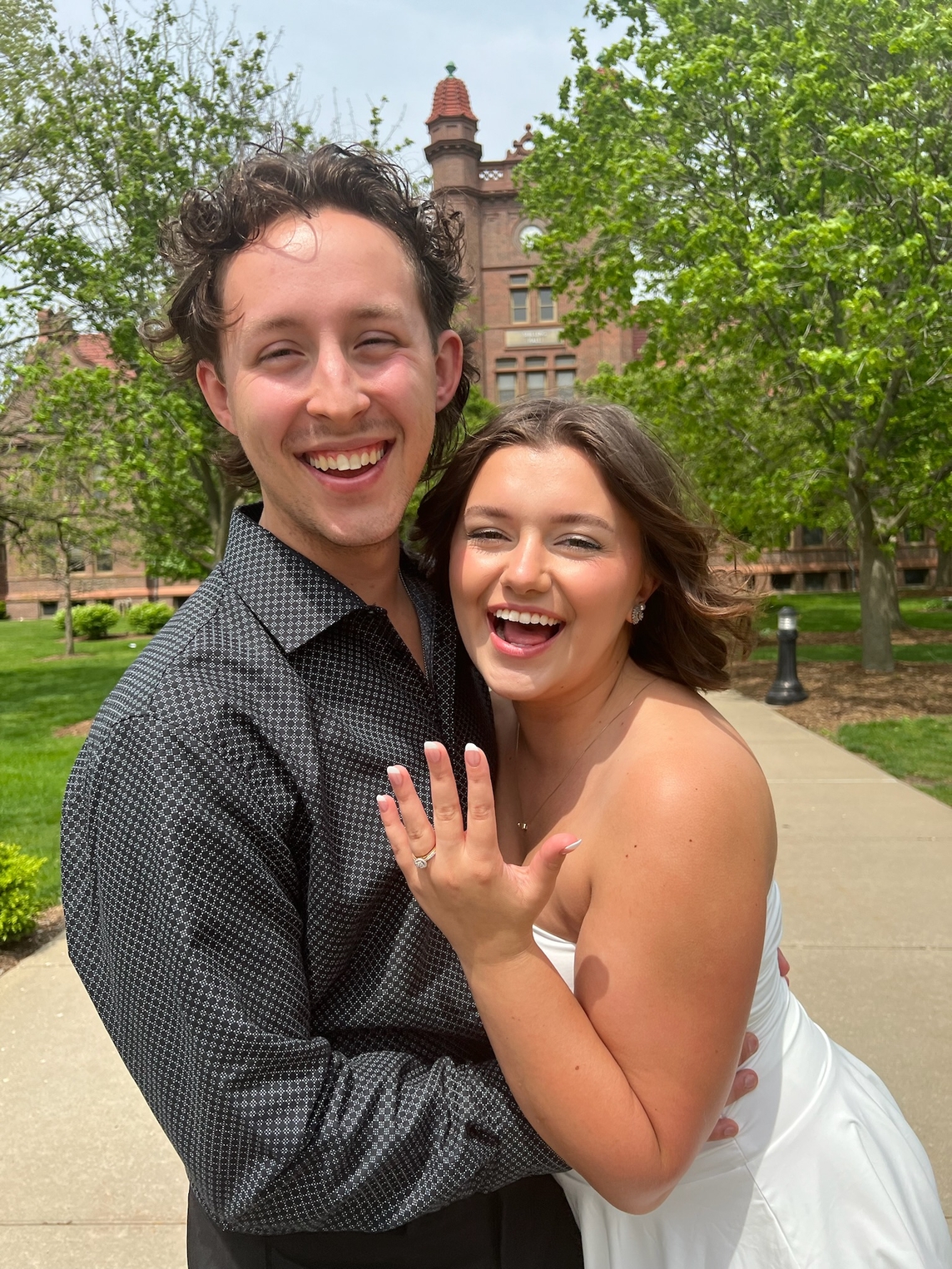 Robbie and MaryHelen stand outside of Shilling Hall showing off MaryHelen's engagement ring after their proposal
