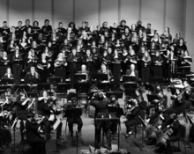 Black and White image of the Millikin Choirs and Orchestra on stage. 