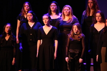 Treble Choir singing in front of black backdrop.