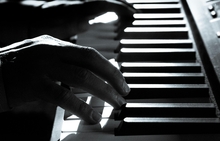 Black and white picture of hands playing a piano keyboard.